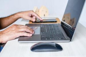 A man sits at a desk and is using a laptop computer. concept working from home, online, use of technology, online shopping, freelancing, internet. Selective focus, closeup, white blurred background. photo
