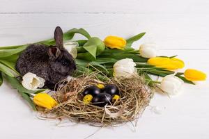 conejito de pascua con huevos de pascua con tulipanes y un nido de heno. composición positiva de pascua de primavera. foto