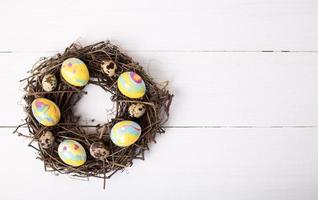 nest with colored easter eggs on white wooden background photo