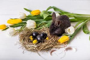 conejito de pascua con huevos de pascua con tulipanes y un nido de heno. composición positiva de pascua de primavera. foto