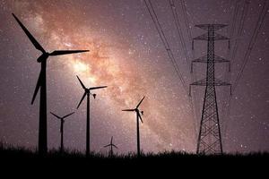 A silhouette of a windmill used to generate electricity in a field against a beautiful Milky Way backdrop. photo