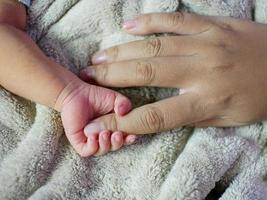Newborn baby grasping her mother's finger. Concept of baby care, feeling safe, parent love. Selective soft focus.