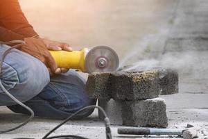 Close up of worker hand using grinder cutting turf stone block for paving sidewalk in public area photo