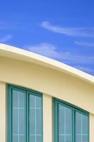 Green glass attic windows on curved roof of modern yellow building against white cloud and blue sky background in vertical frame photo