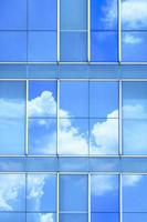 Reflejo de nubes y cielo azul en la superficie de la pared de un edificio moderno de vidrio en un marco vertical foto