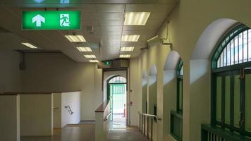 Electric green emergency exit sign on ceiling in empty corridor tunnel of sky train station. photo