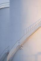 Morning sunshine on curve spiral staircase surface of white storage fuel tanks in vertical frame photo