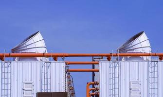 Two large ventilation chimneys with orange pipelines and exhausting machine system on factory building roof against blue sky background photo