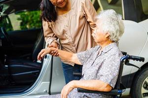 cuidador ayuda a una anciana asiática con discapacidad a entrar en su automóvil, concepto médico. foto