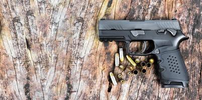 Pistola negra automática de 9 mm y balas sobre una mesa de madera.
