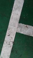 Close up of a chapped-white line drawn on a green-broken floor at public sports field. photo