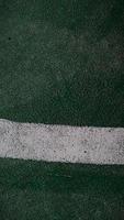 Close up of a chapped-white line drawn on a green-broken floor at public sports field. photo