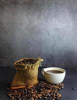 Coffee beans in brown sack bag with coffee cup on black background. photo