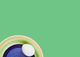 Colorful plate with a white egg isolated on green background. photo