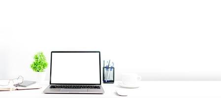 Blank white screen laptop on a white table in the office. A working concept using technology, notebook, smartphones, devices. Copy space on right for design or text, Closeup, Gray, and blur background photo