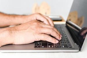 A man sits at a desk and is using a laptop computer. concept working from home, online, use of technology, online shopping, freelancing, internet. Selective focus, closeup, white blurred background. photo