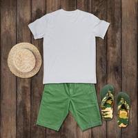 White t-shirt with green shorts, sandals, hat placed on the wooden floor.