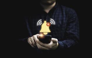 hombre de negocios que sostiene un teléfono inteligente con una campana amarilla virtual que suena para el concepto de alerta de notificación de la aplicación. foto