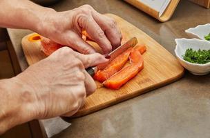 el chef corta el salmón con un cuchillo en tiras para preparar el plato según la receta foto