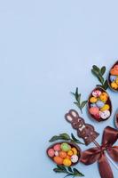 Flat lay Easter hunt concept with chocolate eggs and bunny on blue background. View from above copy space
