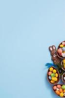 Flat lay Easter hunt concept with chocolate eggs and bunny on blue background. View from above