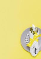 Top view of plate and cutlery and glass with easter egg on yellow background with copy space photo