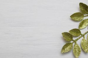 Top view of tree branch with golden glitter leaves on white wooden background photo