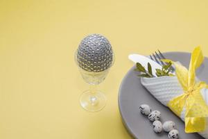 Decorative easter egg in a glass against the background of cutlery in a plate on a yellow background photo
