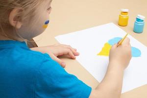 Yellow and blue paints and children's hands with a brush at the table. Drawings of Ukrainian children concept photo