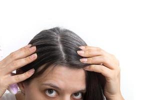 una joven examina el pelo gris de su cabeza en un espejo sobre un fondo blanco. cerrar la textura de las canas foto