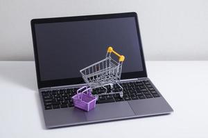 Open laptop with supermarket trolley and basket on the table. Online shopping from home photo