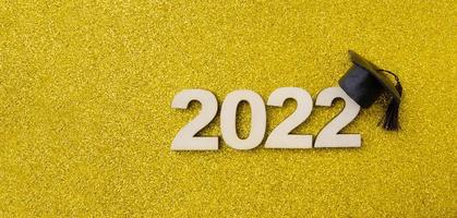 sombrero o gorra graduados con el número de madera 2022 sobre un fondo de brillo amarillo. formato de banner de concepto de clase 2022 foto