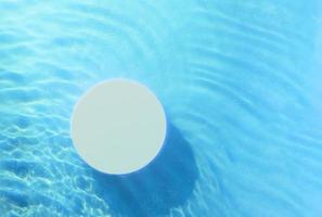 Top view of empty round podium in transparent waves of water on blue background. Blank cosmetic product photo