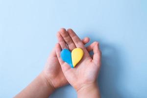 Heart of yellow-blue colors of the national flag of Ukraine in a childs hands, top view. Love for the motherland in the children's heart concept photo