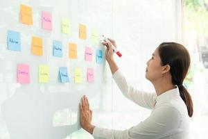 Business manager showing idea for her team and stick many memo paper on glass window to success working in business meeting  creative office, planning and management concept. photo