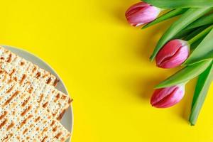 Traditional Jewish food matzo bread and pink tulips on a yellow background. Happy Passover. Religious spring holiday Pesach. Copy space.
