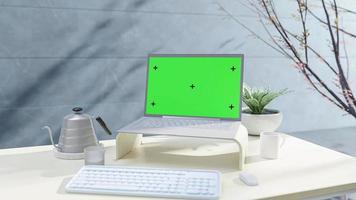Laptop-Attrappe auf Schreibtisch neben Wand mit Pflanze daneben. Seitenlicht beschattet den Baum. selektiver fokus auf dem bildschirm. grüner bildschirm für banner und logo. Animation, 3D-Darstellung.