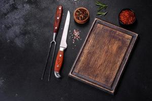Brown rectangular wooden cutting board with salt and spices on a dark concrete background photo