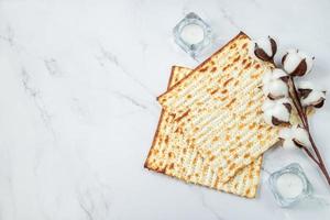 Happy Passover concept. Matzo bread and cotton flowers on a white marble. Background religious Jewish holiday Pesach. Copy space. photo