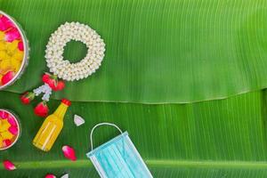 fondo del festival songkran con flores de guirnalda de jazmín en un tazón de agua, perfume y piedra caliza sobre un fondo verde de hoja de plátano húmedo. foto