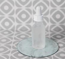 Cosmetic glass bottle with pipette on tile background photo