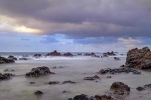 Evening on the Atlantic Ocean - On the north coast of Tenerife. Long exposure Half an hour before sunset, low tide, the water of the sea has retreated The rugged rocks overgrown with algae are exposed photo