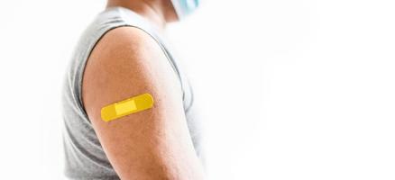 The yellow plaster is attached to the man's arm. Concept for first aid after coronavirus COVID-19 vaccination, and professional, medical, needle, blood, cancer. Closeup, white blurred background photo