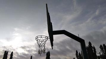 vista lateral del antiguo aro de baloncesto verde tenue y red rota con un fondo oscuro del cielo matutino en el campo deportivo público. foto