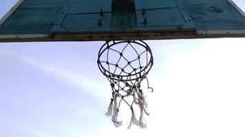 Bottom view of dim green old basketball hoop and broken net with a dark background of morning sky in the public sport field.