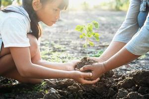 children and mom helping planting young tree. eco concept photo