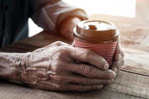 Hands of old man holding cup of coffee on the wood table. photo