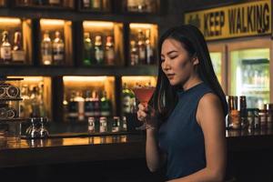mujer asiática bebiendo un cóctel en un bar por la noche. foto