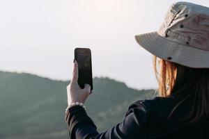 Asian female tourists use their mobile phones to take pictures of the scenery at the top of a fresh mountain hill. photo