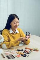 Young asian woman vlogging about cosmetics skin care items products on table with her video camera and demonstrates product use and reviews for her online blog channel. photo